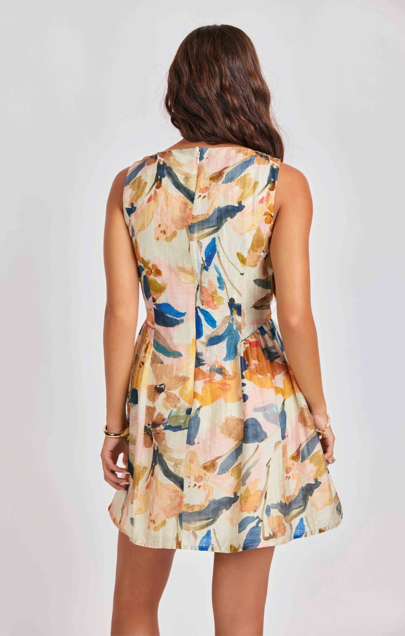 Woman wearing a sleeveless floral dress against a plain background