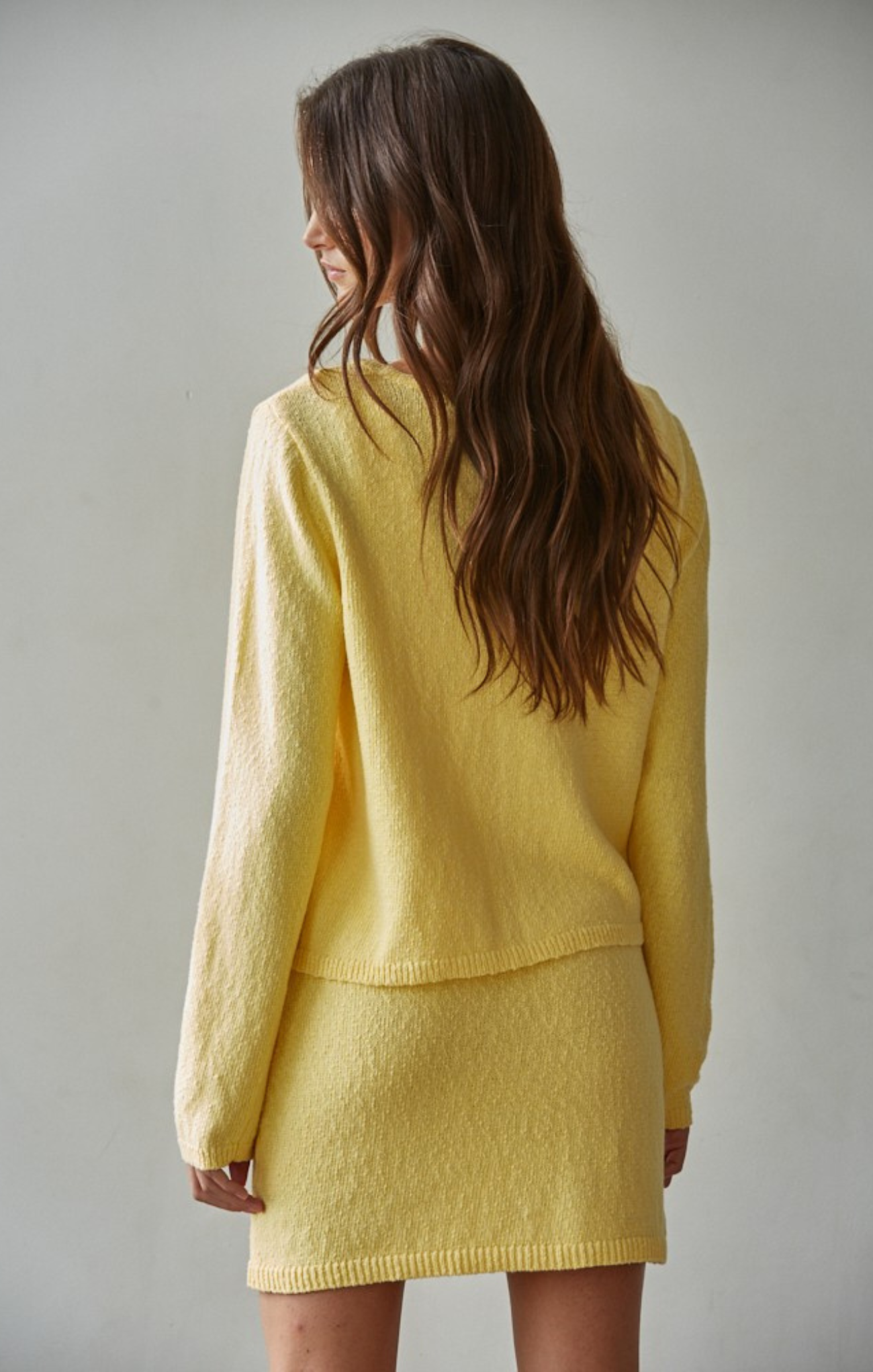 Woman wearing a yellow knitted outfit against a plain background