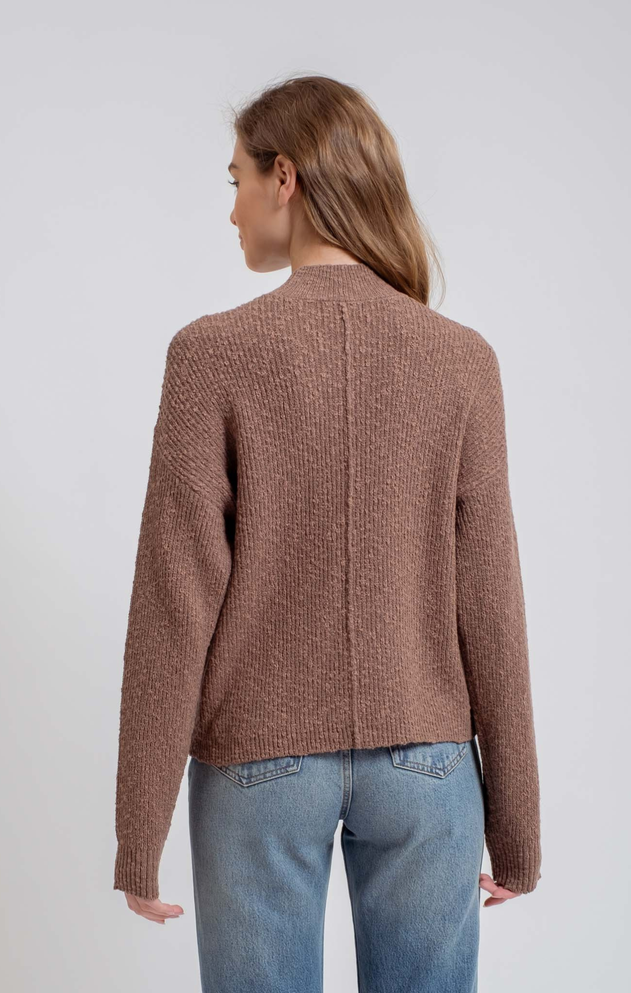 Woman wearing a brown knitted cardigan and blue jeans on a light gray background