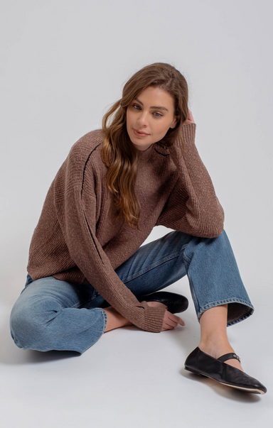 Woman wearing a brown sweater and blue jeans sitting on a white background