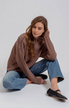 Woman wearing a brown sweater and blue jeans sitting on a white background