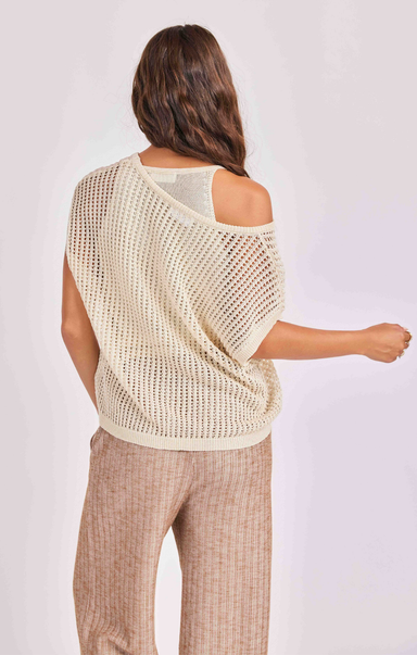 Woman wearing a beige knit top and beige pants on a light background