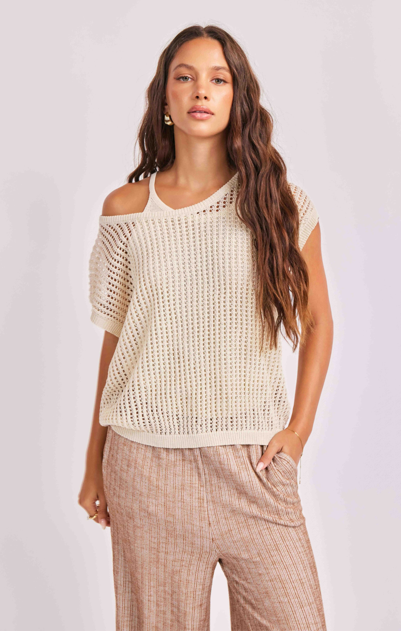 Woman wearing a beige crochet top and plaid pants on a white background