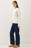 Woman wearing a white cable knit sweater and dark blue jeans on a white background