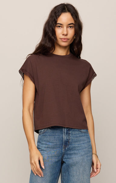 Woman wearing a brown t-shirt and blue jeans against a beige background