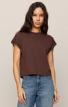 Woman wearing a brown t-shirt and blue jeans against a beige background