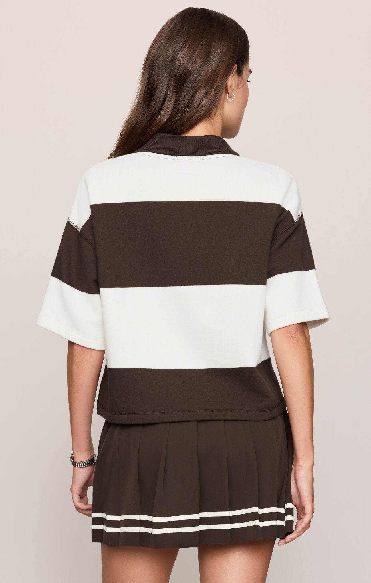 A woman shown from the back wearing a color-blocked short-sleeve top and pleated mini skirt set. The set features horizontal stripes in dark brown and off-white, with matching striped trim on the hem of the skirt.