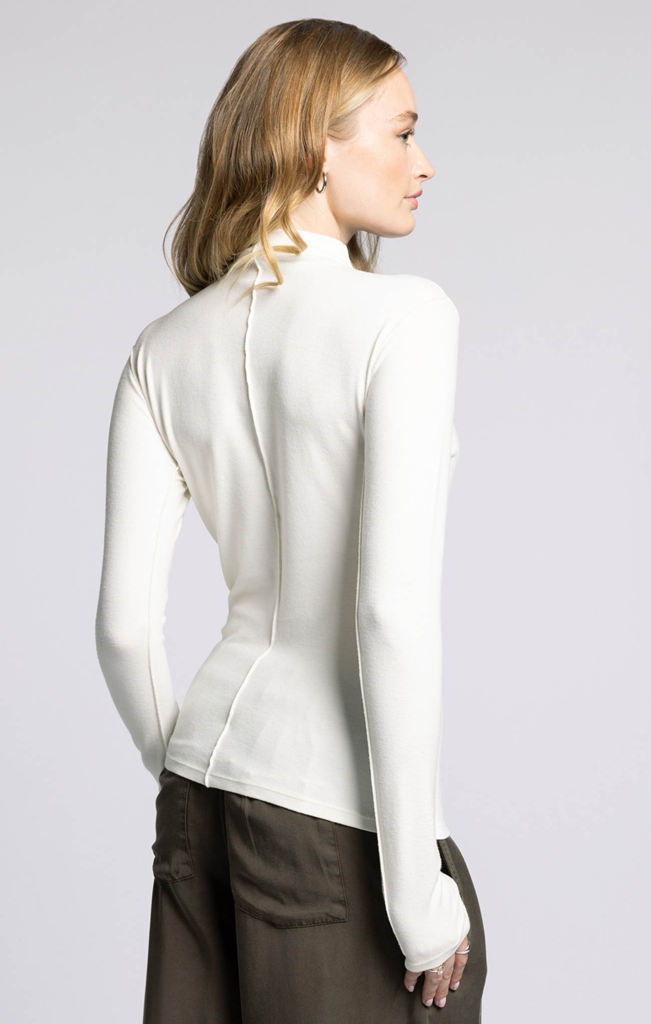 Woman wearing a white long-sleeve top against a plain background