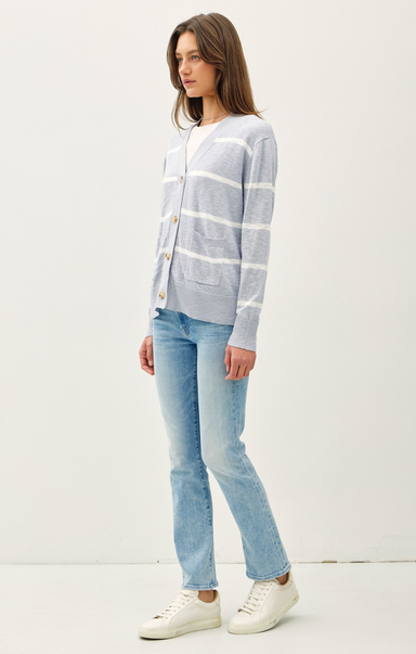 Woman wearing a striped cardigan, jeans, and white sneakers on a white background