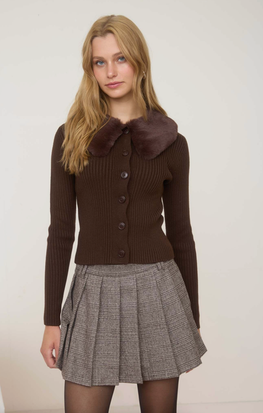 Woman wearing a brown sweater with a fur collar and a plaid skirt on a white background