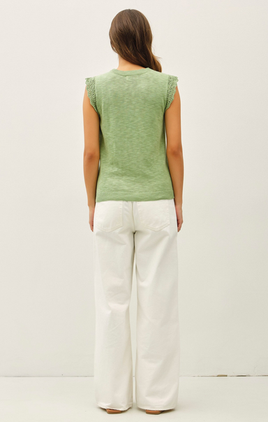 Woman wearing a green sleeveless top and white pants on a light background
