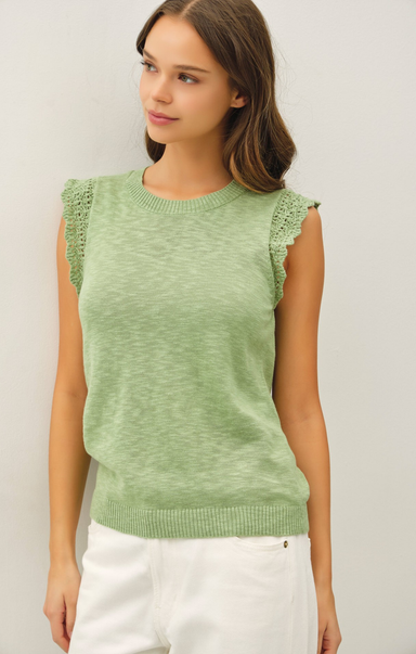 Woman wearing a green sleeveless knitted top with ruffled shoulders against a plain background