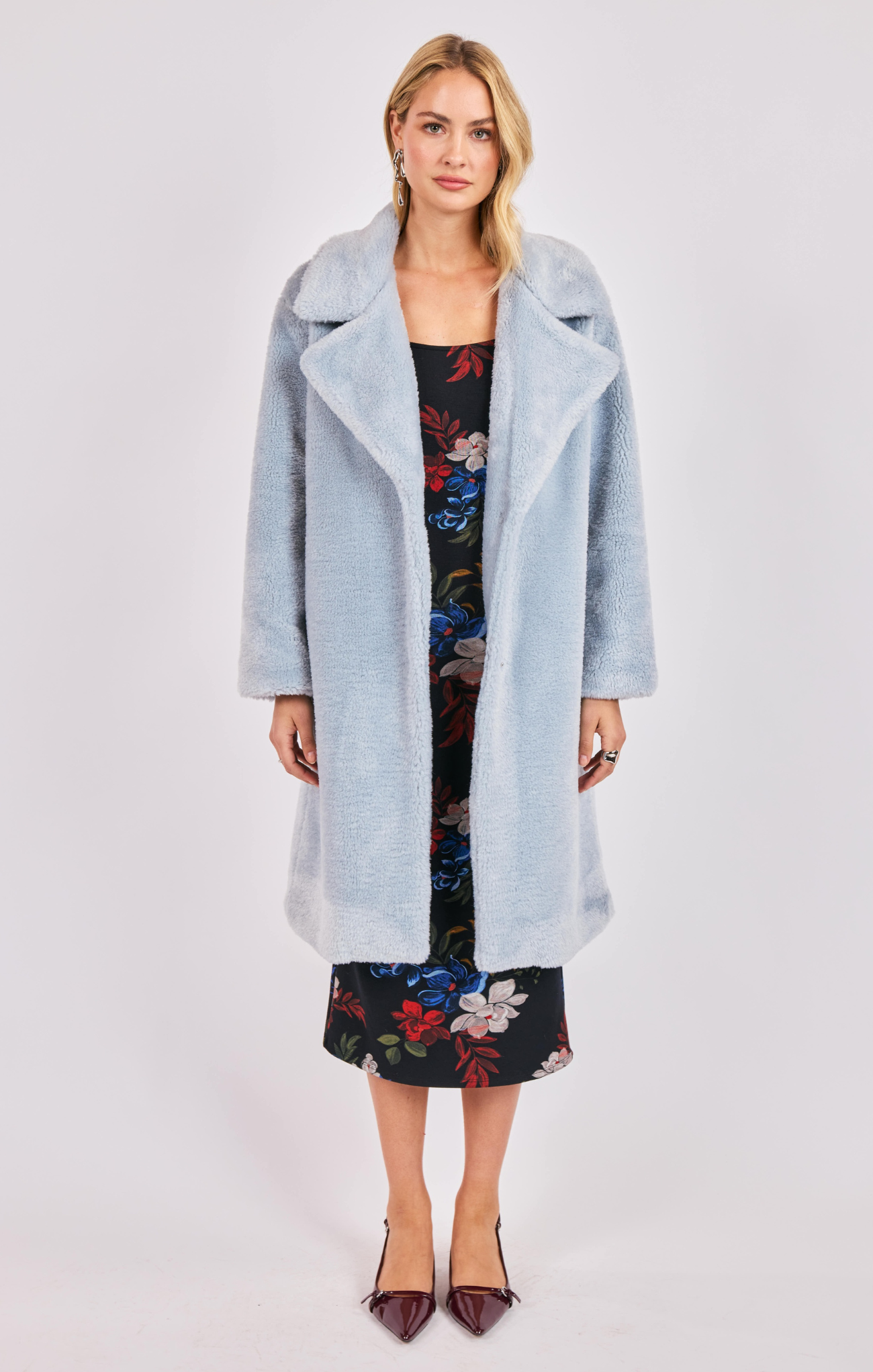 Woman wearing a light blue coat over a floral dress on a white background