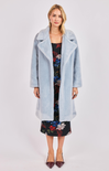 Woman wearing a light blue coat over a floral dress on a white background