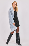 Woman wearing a light blue coat, black dress, and black knee-high boots on a white background