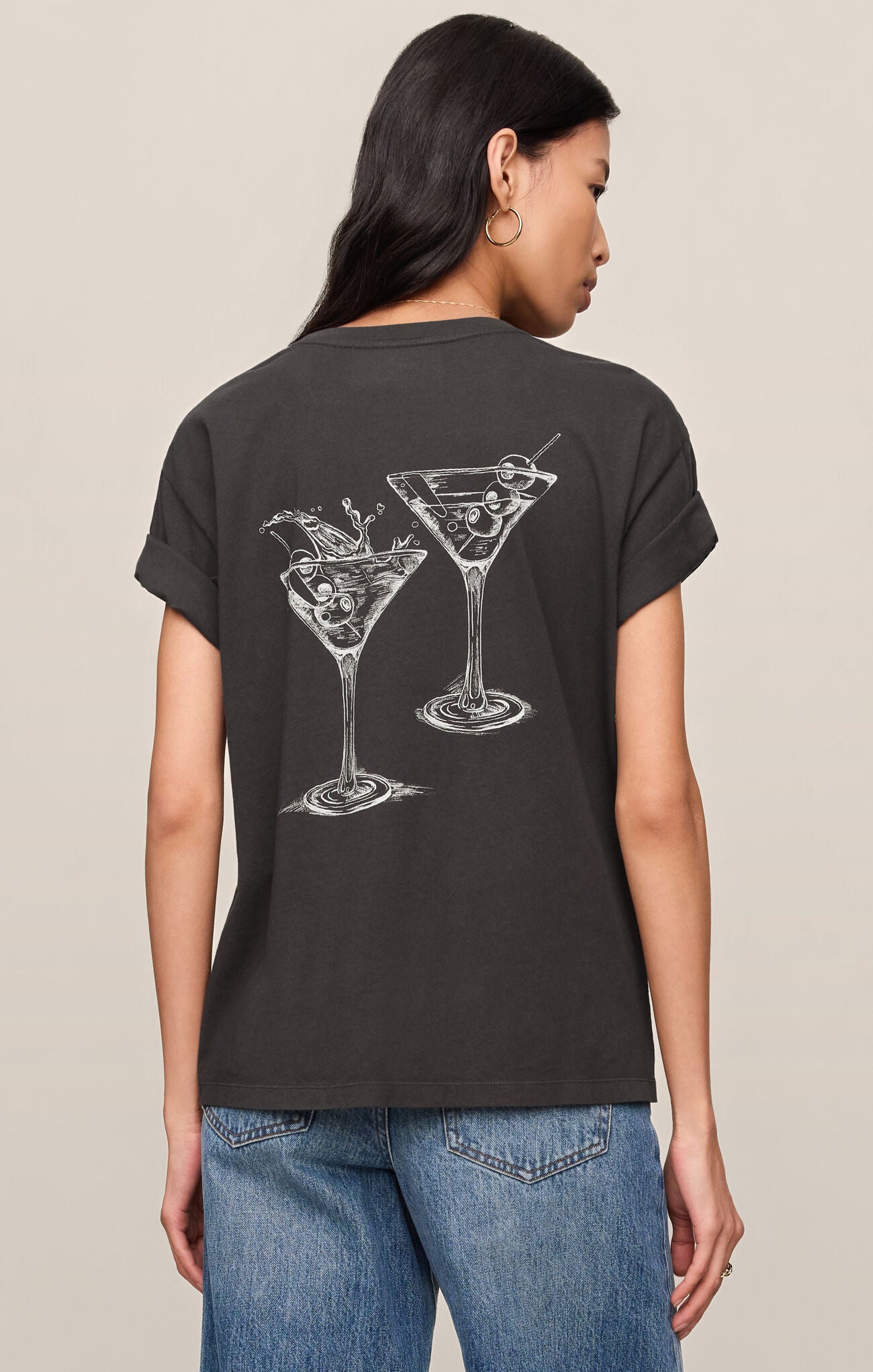 Person wearing a black t-shirt with martini glass designs on the back, standing against a beige background.