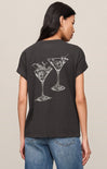 Person wearing a black t-shirt with martini glass designs on the back, standing against a beige background.