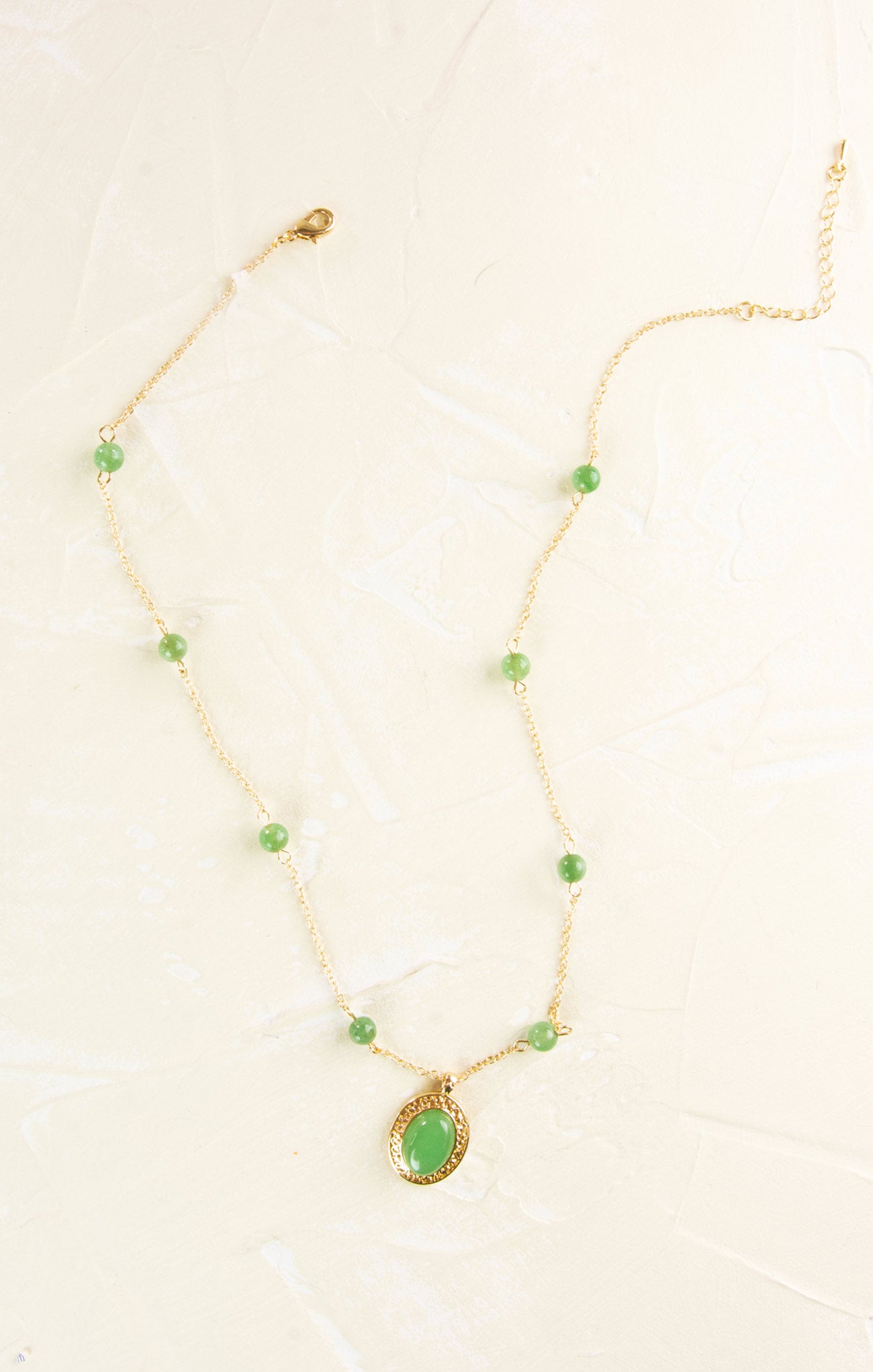Gold necklace with green teardrop pendant on a white background