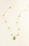 Gold necklace with green teardrop pendant on a white background