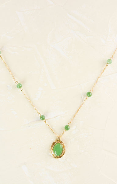 Gold necklace with a green pendant on a light background