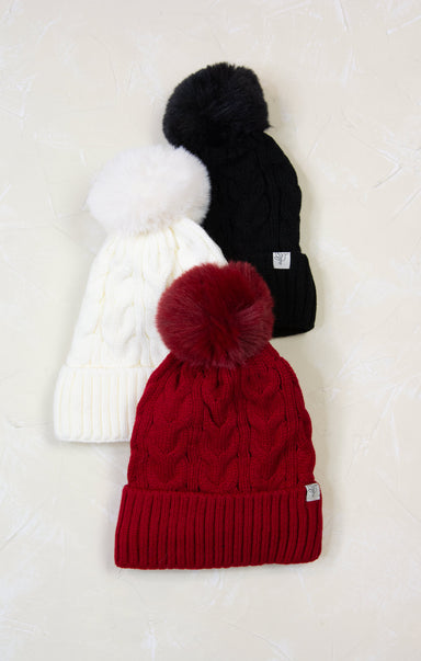 Three knit hats with pom-poms in red, white, and black on a light background
