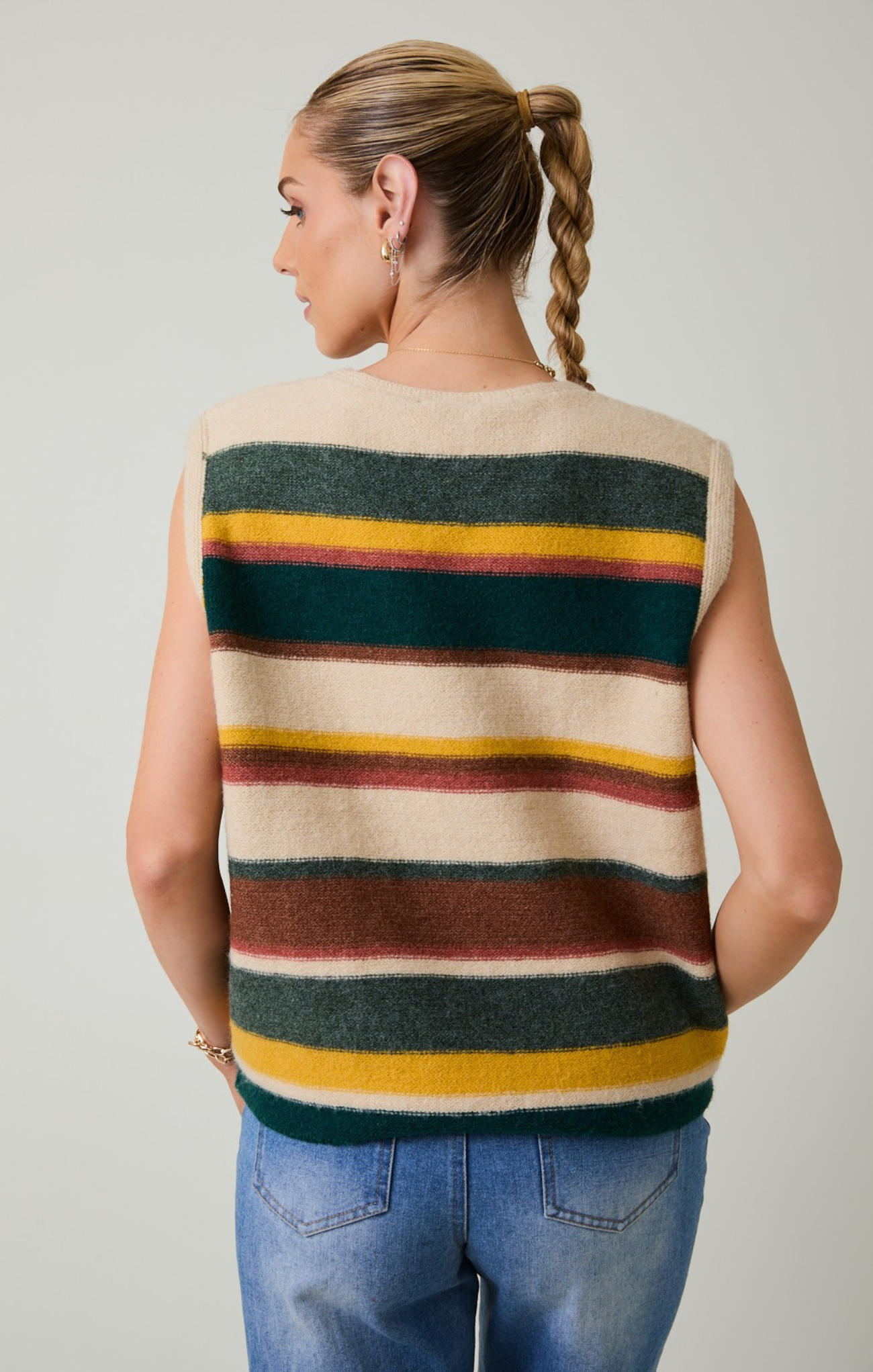 Woman wearing a sleeveless, multicolored striped sweater against a plain background