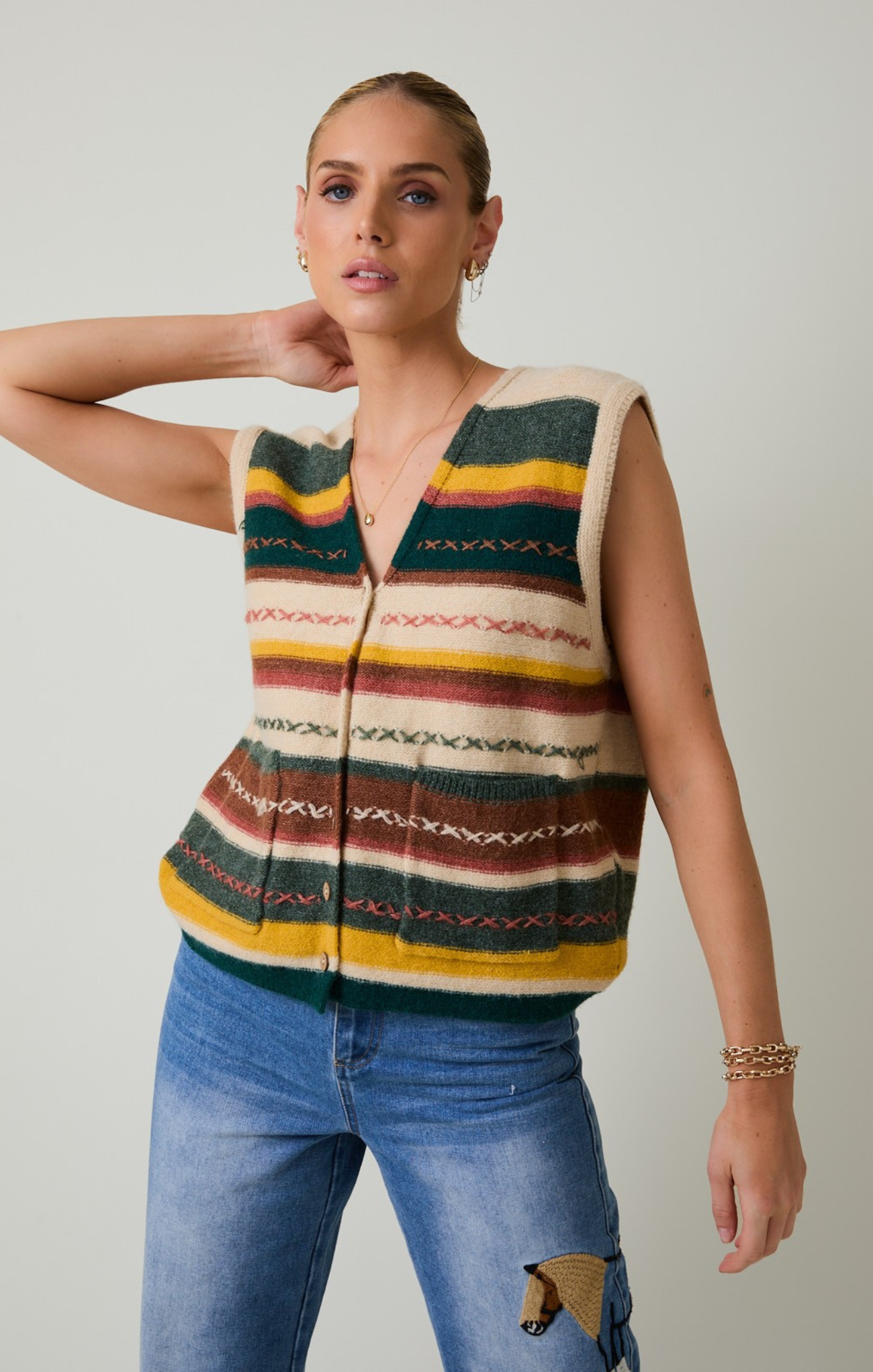 Woman wearing a colorful striped vest and blue jeans against a plain background