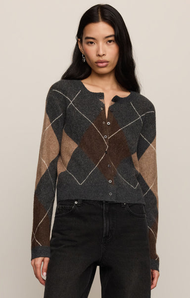 Woman wearing a patterned sweater and black pants on a plain background