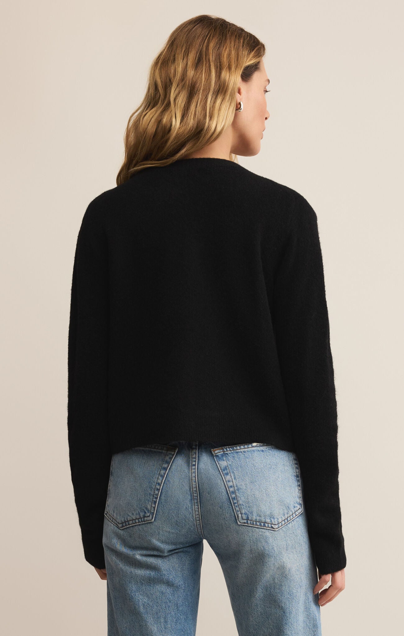 Person wearing a black sweater and blue jeans on a beige background
