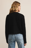Person wearing a black sweater and blue jeans on a beige background