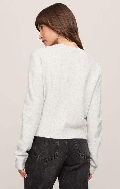 Woman wearing a light gray sweater and dark jeans on a beige background