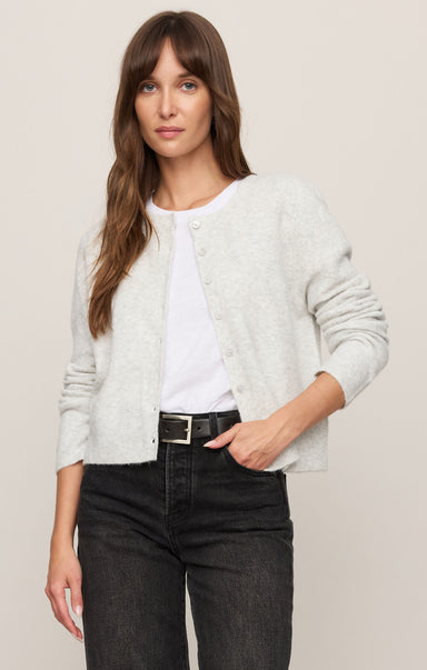Woman wearing a light gray cardigan over a white shirt with black pants on a beige background