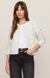 Woman wearing a light gray cardigan over a white shirt with black pants on a beige background