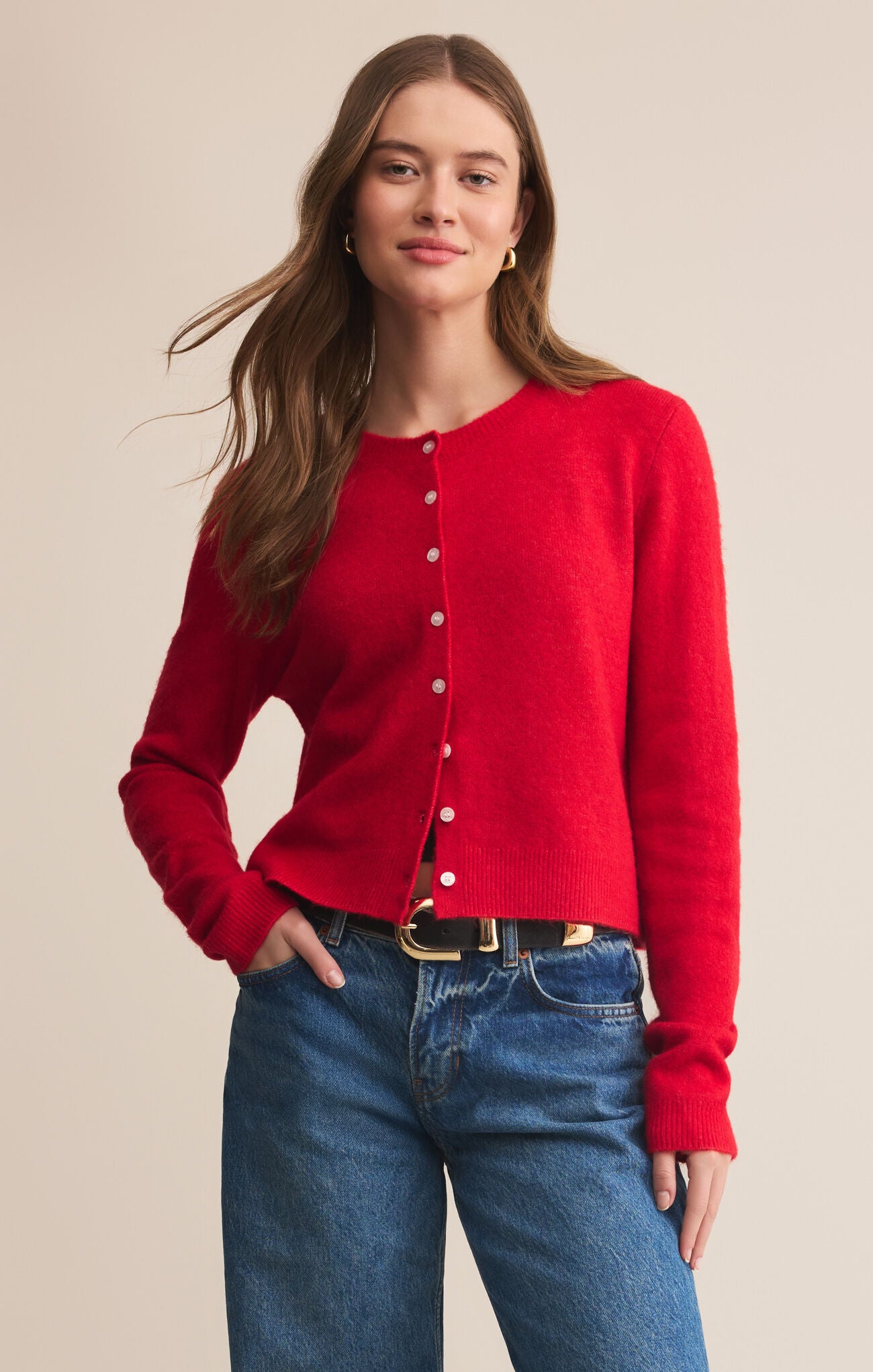 Woman wearing a red cardigan and blue jeans against a beige background
