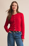 Woman wearing a red cardigan and blue jeans against a beige background
