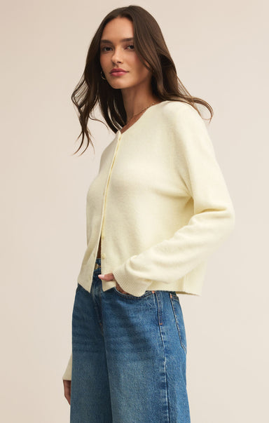 Woman wearing a light yellow cardigan and blue jeans against a beige background