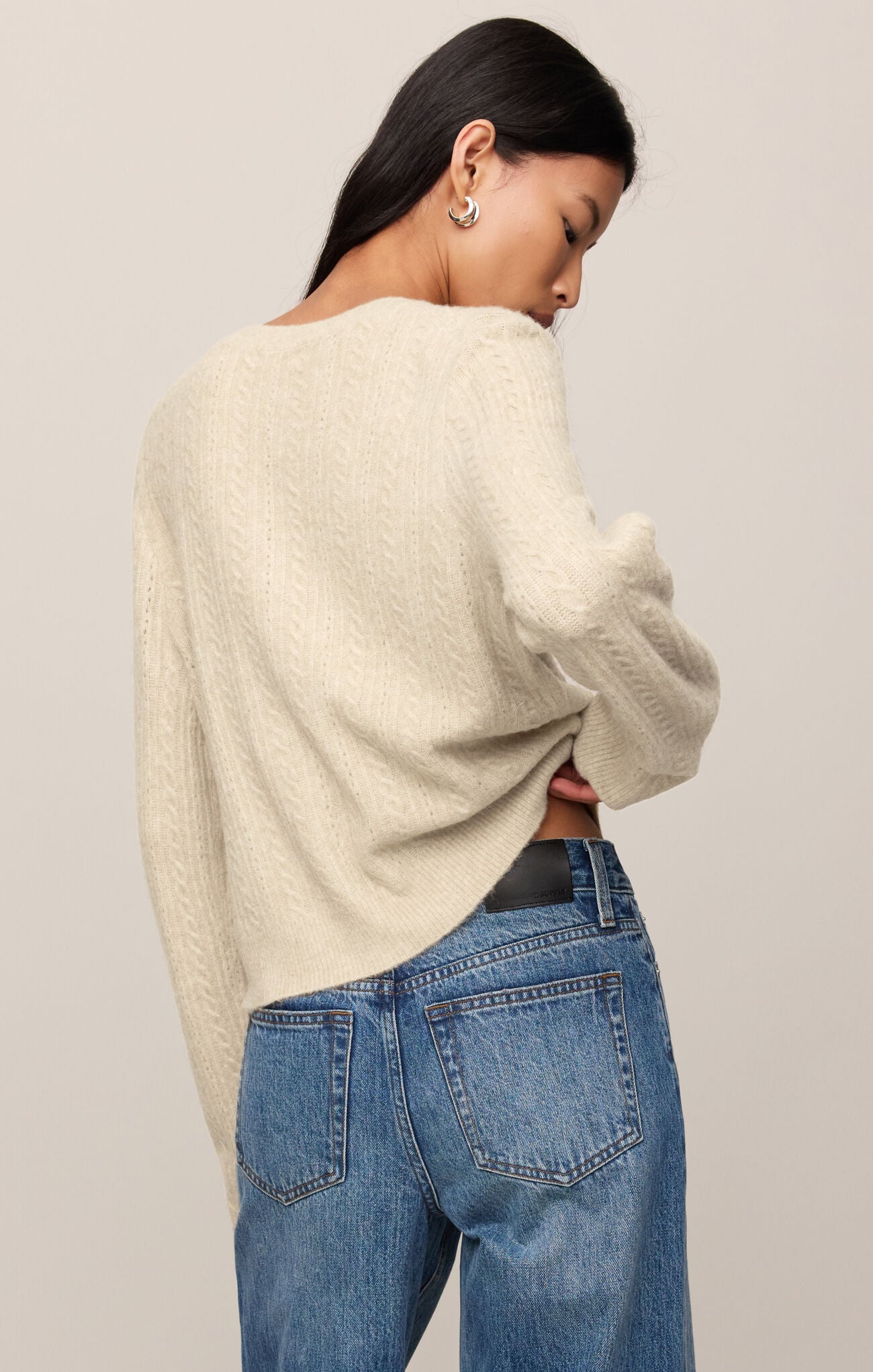 Person wearing a cream sweater and blue jeans against a plain background