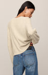 Person wearing a cream sweater and blue jeans against a plain background