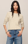 Woman wearing a beige cardigan and blue jeans against a plain background