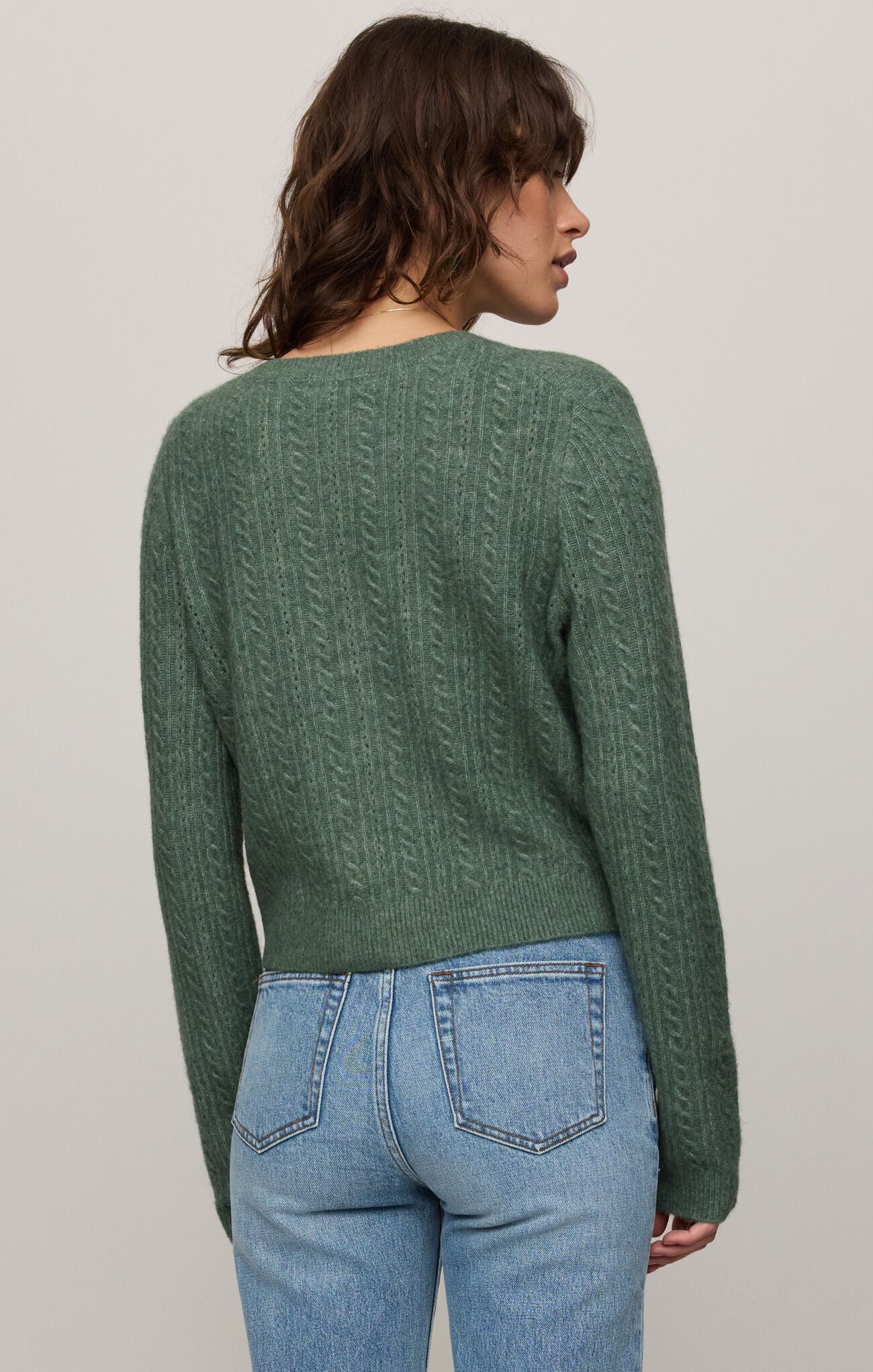 Person wearing a green sweater and blue jeans against a plain background