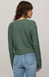 Person wearing a green sweater and blue jeans against a plain background