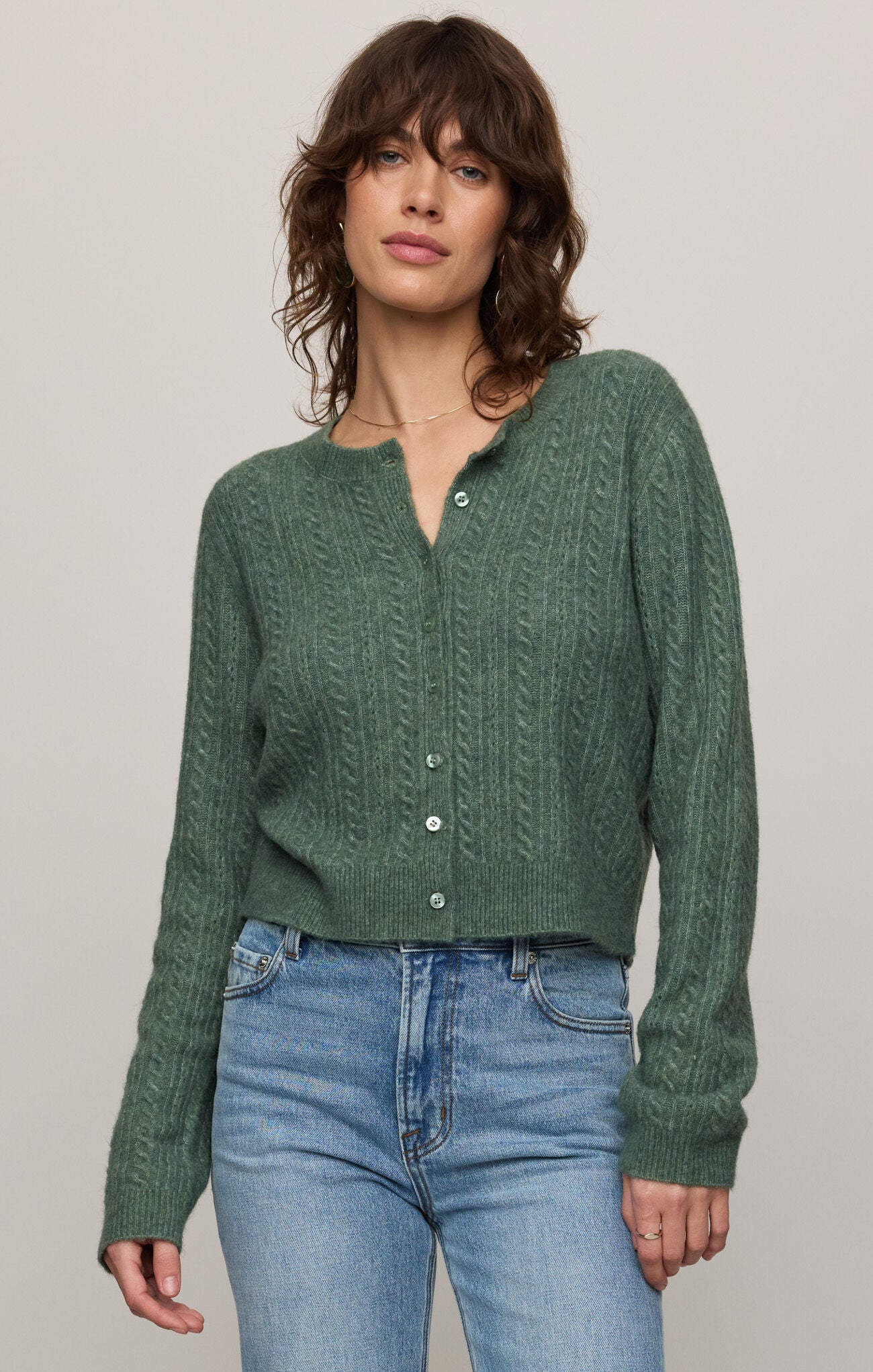 Woman wearing a green knitted cardigan and blue jeans against a plain background