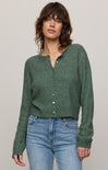 Woman wearing a green knitted cardigan and blue jeans against a plain background