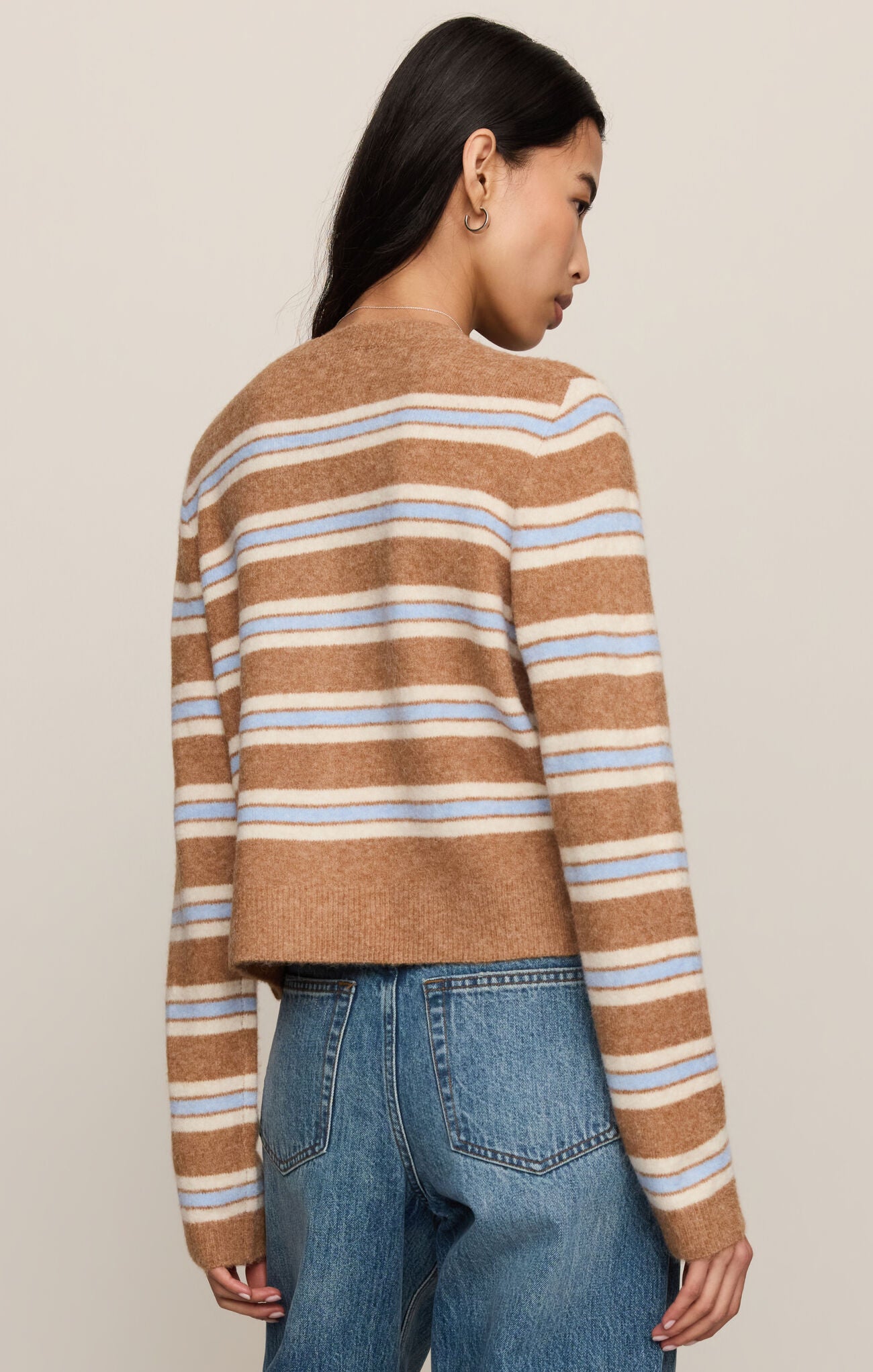 Person wearing a brown and blue striped sweater with blue jeans on a beige background