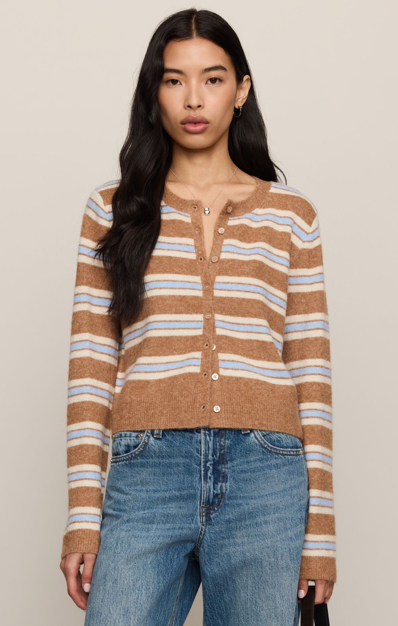 Woman wearing a brown and blue striped sweater with blue jeans against a beige background