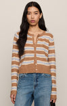 Woman wearing a brown and blue striped sweater with blue jeans against a beige background