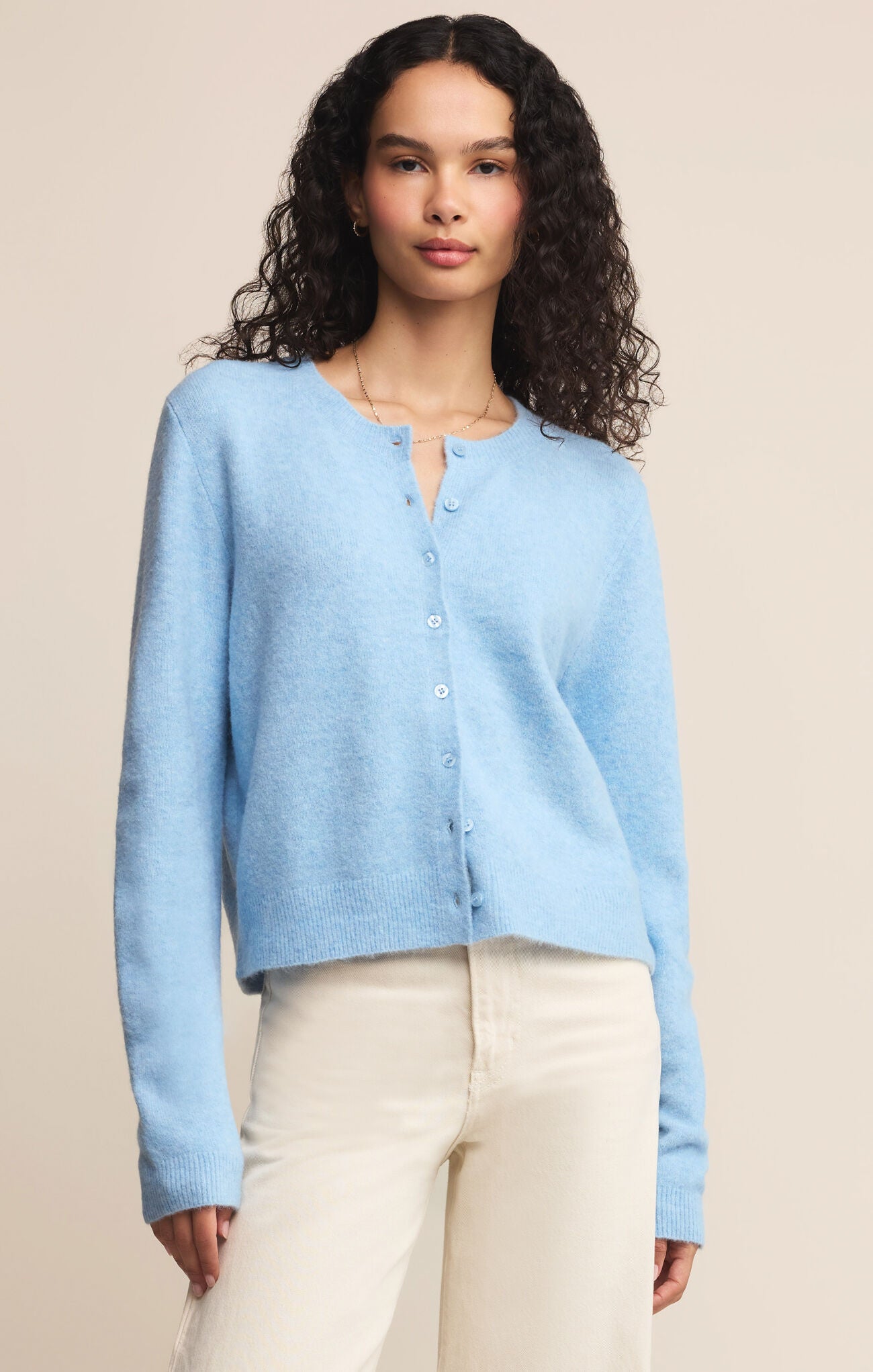 Woman wearing a light blue cardigan over a white top with beige pants on a beige background
