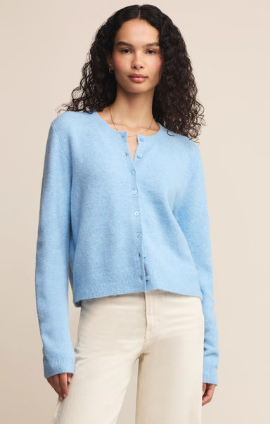 Woman wearing a light blue cardigan over a white top with beige pants on a beige background