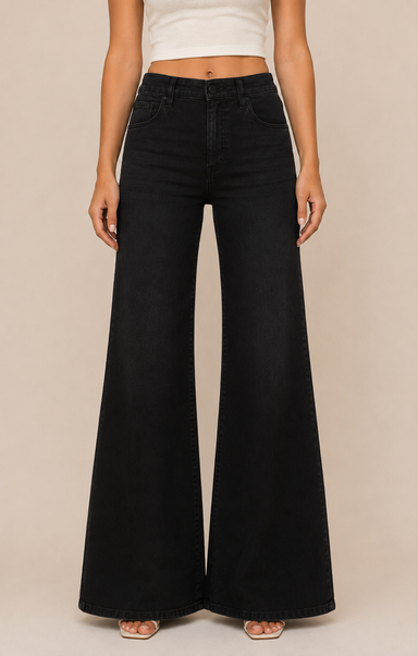 A model wearing black wide-leg flare jeans, paired with a white crop top and beige flat sandals, standing against a solid beige studio background.