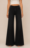 A model wearing black wide-leg flare jeans, paired with a white crop top and beige flat sandals, standing against a solid beige studio background.